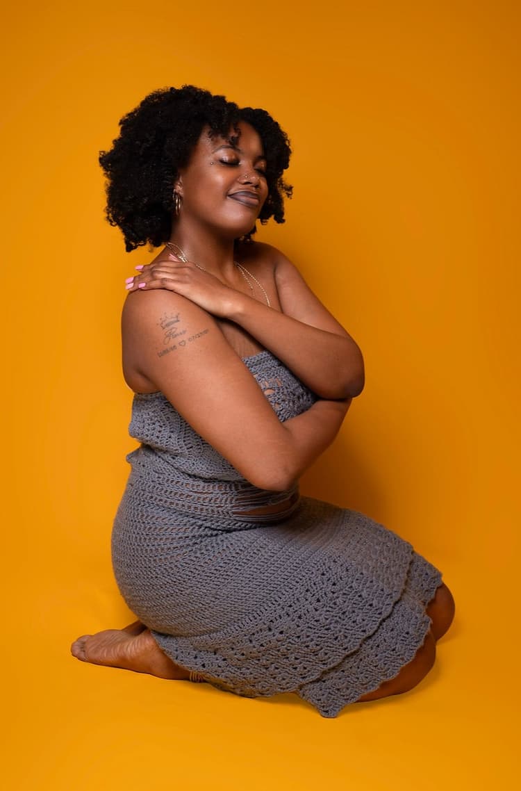 a photo of me in a crochet grey dress against a yellow background.